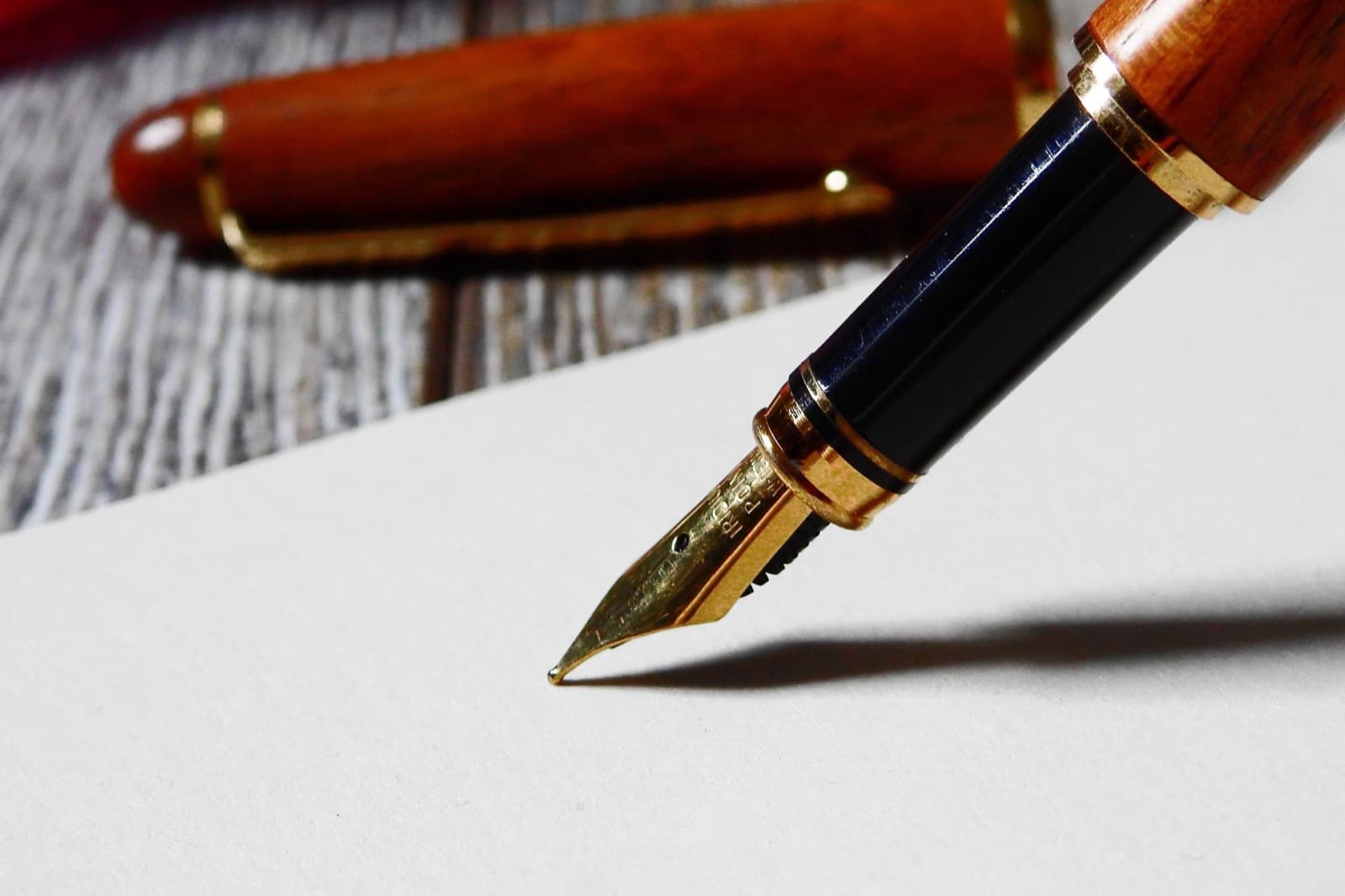 Pluma estilográfica de madera y una hoja de papel en blanco sobre un escritorio.