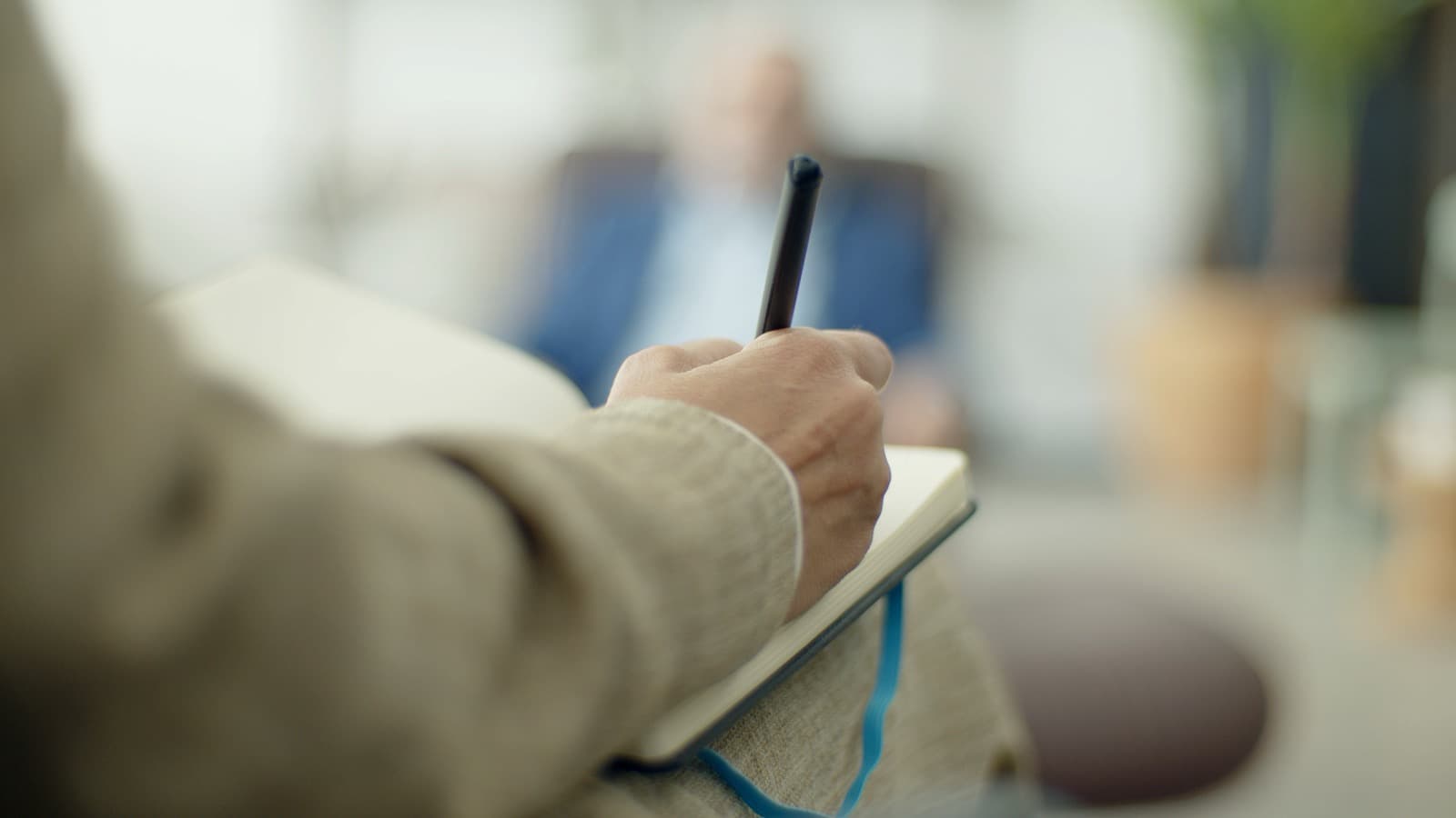 Mano tomando notas en un cuaderno durante una conversación, con el fondo fuera de foco